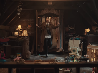 Screengrab from John Lewis Christmas ad 2024, showing a woman walking into a dimly lit attic filled with toys and lamps